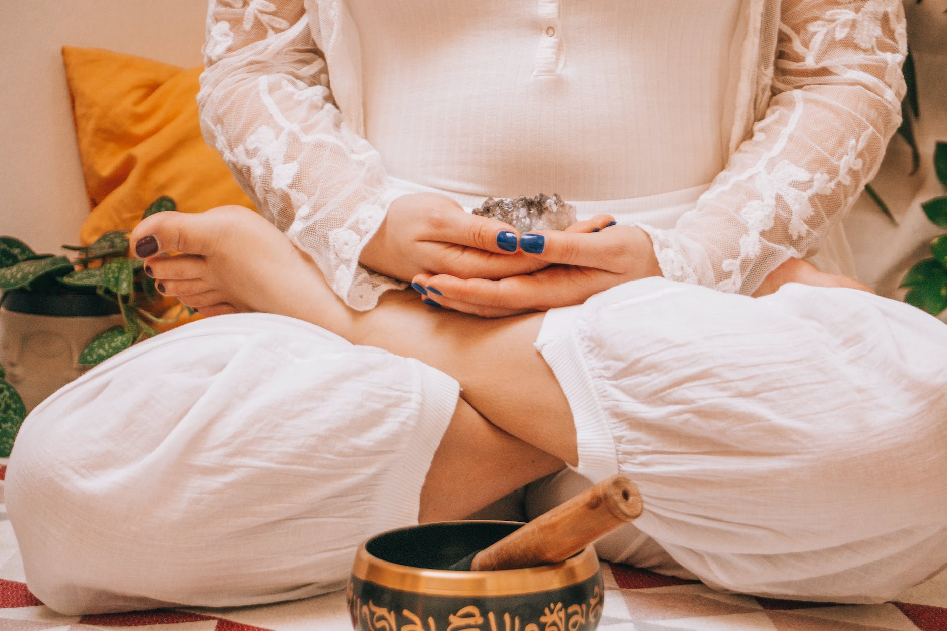 a woman in lotus position holding a crystal sitting near a metal bowl